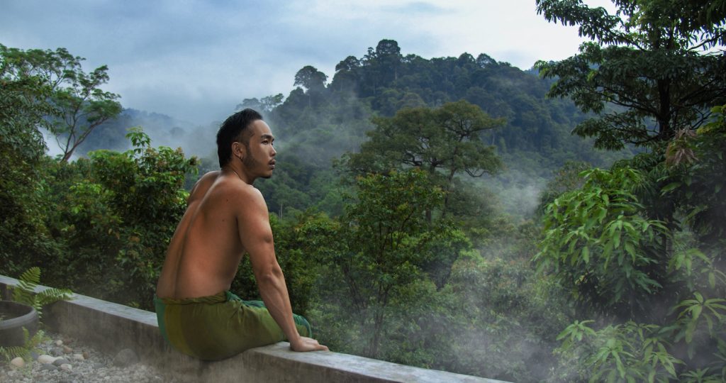A man looking out into the misty Malaysian rainforest.