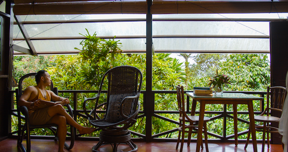 A woman sitting in a rocking chair on a balcony overlooking houses.